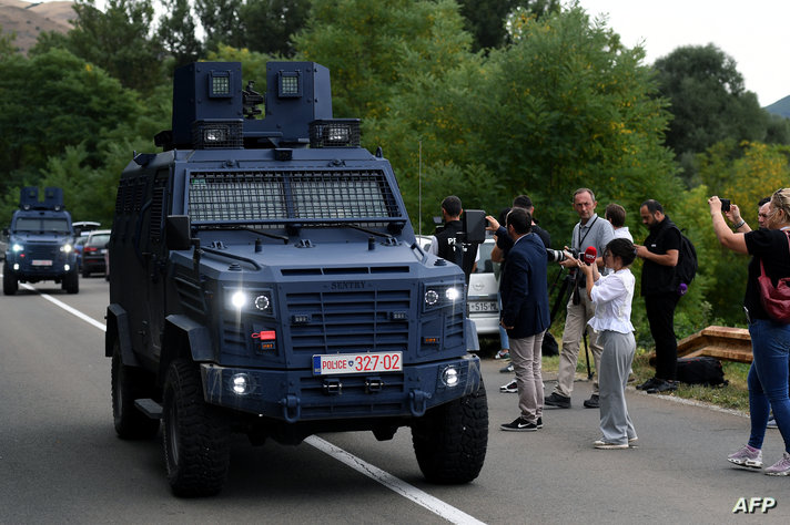 Kosovo's police vehicles drive past members of the public taking photographs near the entrance of the village of Banjska on…