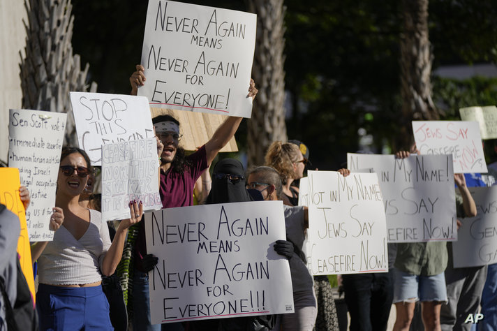 Maymoonah Robinson, a Brazilian Muslim woman wearing a niqab, holds a sign reading "Never Again Means Never Again for Everyone,…