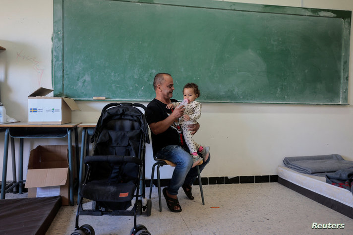 Mohammed Hassan, 52, who said he escaped from the south Lebanese village of Aitaroun, near the Israeli border, gives a feeding bottle to his daughter Danna, as he speaks to her, at a school where they take refuge in Tyre