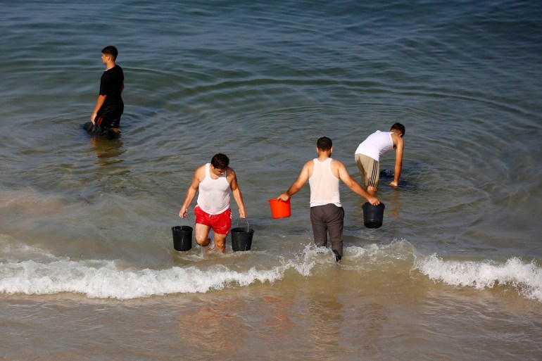 Men fill buckets of seawater to use for washing their clothes east of Deir al-Balah in the central Gaza Strip [Ashraf Amra/Al Jazeera]