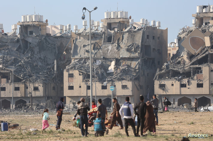 Building lie in ruin as Palestinians carry their belongings following Israeli strikes on residential buildings at the Qatari-funded Hamad City in Khan Younis