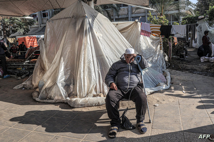 A man dozes while leaning on a crutch as he sits outside a tent where displaced Palestinians are camped outside the European…