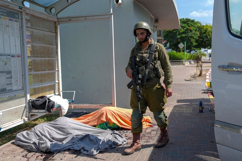 An Israeli soldier stands by the bodies of Israelis killed by Palestinian armed militants who entered from the Gaza strip, in the southern Israeli city of Sderot, Saturday, Oct. 7, 2023. Hamas, the militant group ruling the Gaza Strip, carried out a surprise, multi-front attack on Israel at daybreak Saturday, firing thousands of rockets and infiltrating the country by land, air and sea. (AP Photo/Tsafrir Abayov)