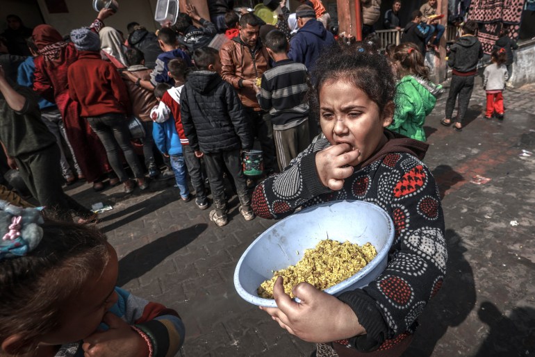 Displaced Palestinian children gather to receive food at a government school in Rafah in the southern Gaza Strip on February 19, 2024, amid the ongoing battles between Israel and the militant group Hamas. (Photo by MOHAMMED ABED / AFP)