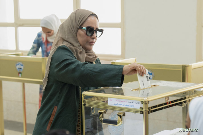 A Kuwaiti citizen drops her ballot into a transparent box after voting to elect new candidates for members of Parliament, in Kuwait City