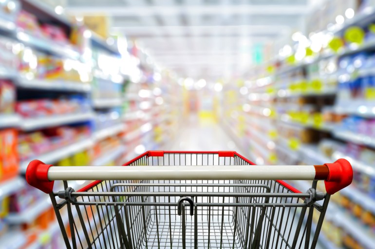 Supermarket aisle with empty red shopping cart.