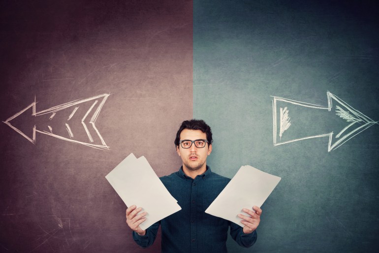 Perplexed businessman has to choose as holds different paper documents in both hands. Selecting the correct financial report, arrows shows left and right sides. Difficult decision, doubt concept.; Shutterstock ID 1754584295; purchase_order: aljazeera ; job: ; client: ; other: