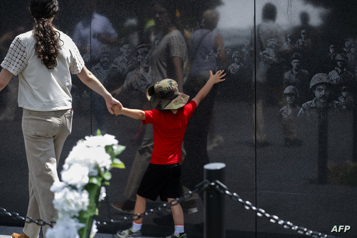 A child reaches out to touch images of soldiers etched on a remembrance wall at the Korea War Memorial at the National Mall…