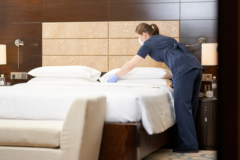 Housemaid standing near bed while cleaning the room in hotel