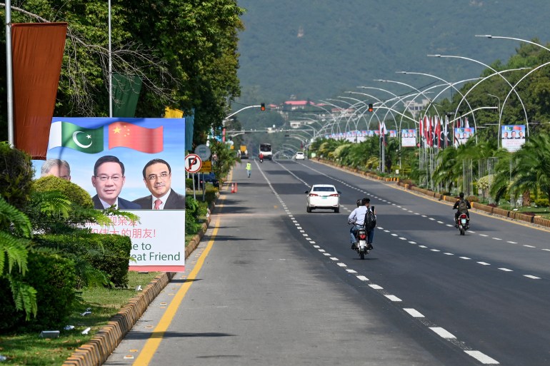 Commuters ride past a billboard featuring images of China's Premier Li Qiang (C), Pakistan's Prime Minister Shehbaz Sharif and President Asif Ali Zardari (R) ahead of the Shanghai Cooperation Organisation (SCO) summit in Islamabad on October 13, 2024. - Pakistan authorities were on October 13 preparing to shut down the capital ahead of a Shanghai Cooperation Organisation summit, overshadowed by recent militant violence and political unrest. (Photo by Aamir QURESHI / AFP)