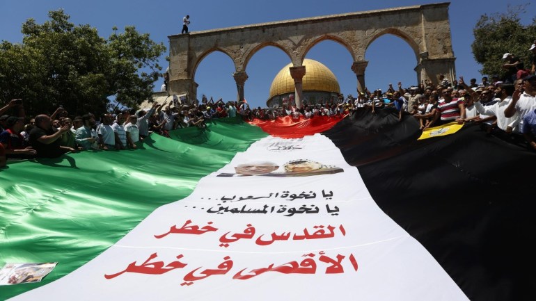 Palestinian worshipers hold a giantr Palestine flag reading 'Jerusalem in danger' after they pray outside the Dome of the Rock at the al-Aqsa mosque compound in Jerusalem during the last Friday prayers of the Muslims' Holy month of Ramadan, 10 July 2015. Most Muslims around the world are observing the holy fasting month of Ramadan, celebrated with prayers and readings from the Koran, and gatherings with family and friends as they abstain from eating, drinking, smoking and sexual relations from dawn till dusk.