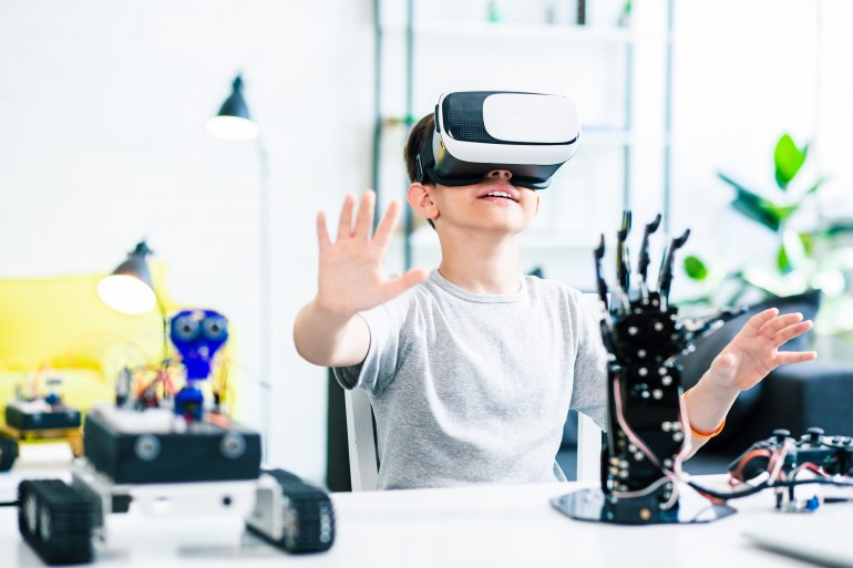 Nice smart enthusiastic boy sitting at the table and wearing VR glasses while experimenting with his robotic devices; Shutterstock ID 1213293706; Department: -