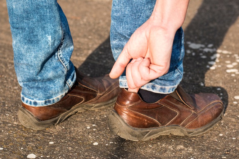 Tight shoe. Man's hand adjusting brown leather shoe on his foot المصدر: أدوبي ستوك