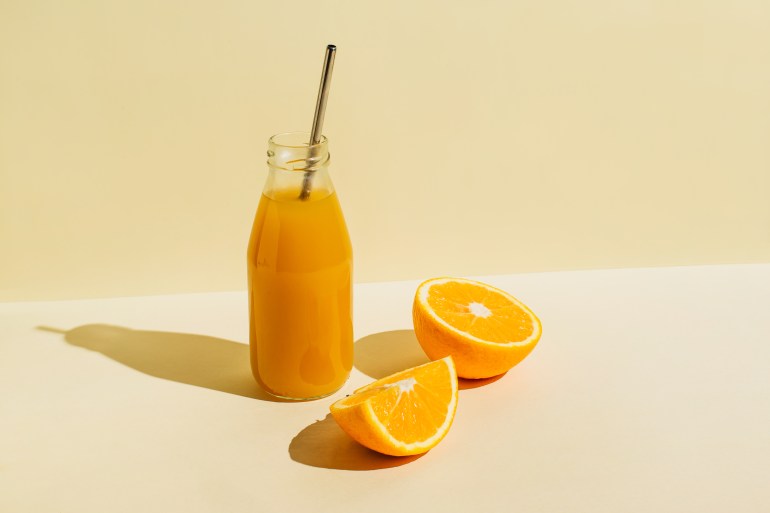 Colorful bottle of freshly squeezed orange juice with fresh ingredients oranges on beige background. Superfoods, healthy food, drinks, diet and detox concept. Flat lay, top view, copy space