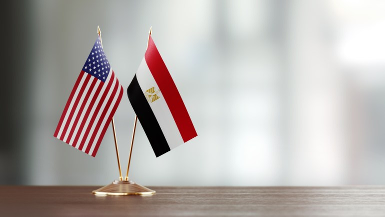 American and Egyptian flag pair on desk over defocused background. Horizontal composition with copy space and selective focus.