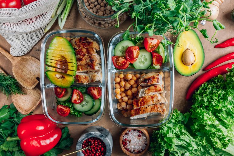 Healthy meal prep containers with chickpeas, chicken, tomatoes, cucumbers and avocados. Healthy lunch in glass containers on beige rustic background. Zero waste concept. Selective focus. المصدر: أدوبي ستوك